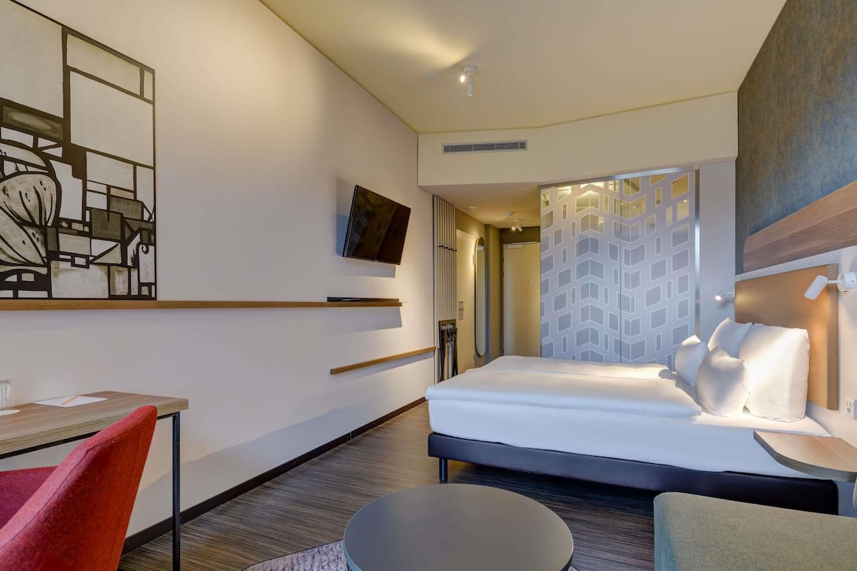 Une chambre d’hôtel moderne équipée d’un lit, d’un bureau, d’une chaise, d’une table ronde et d’un téléviseur.