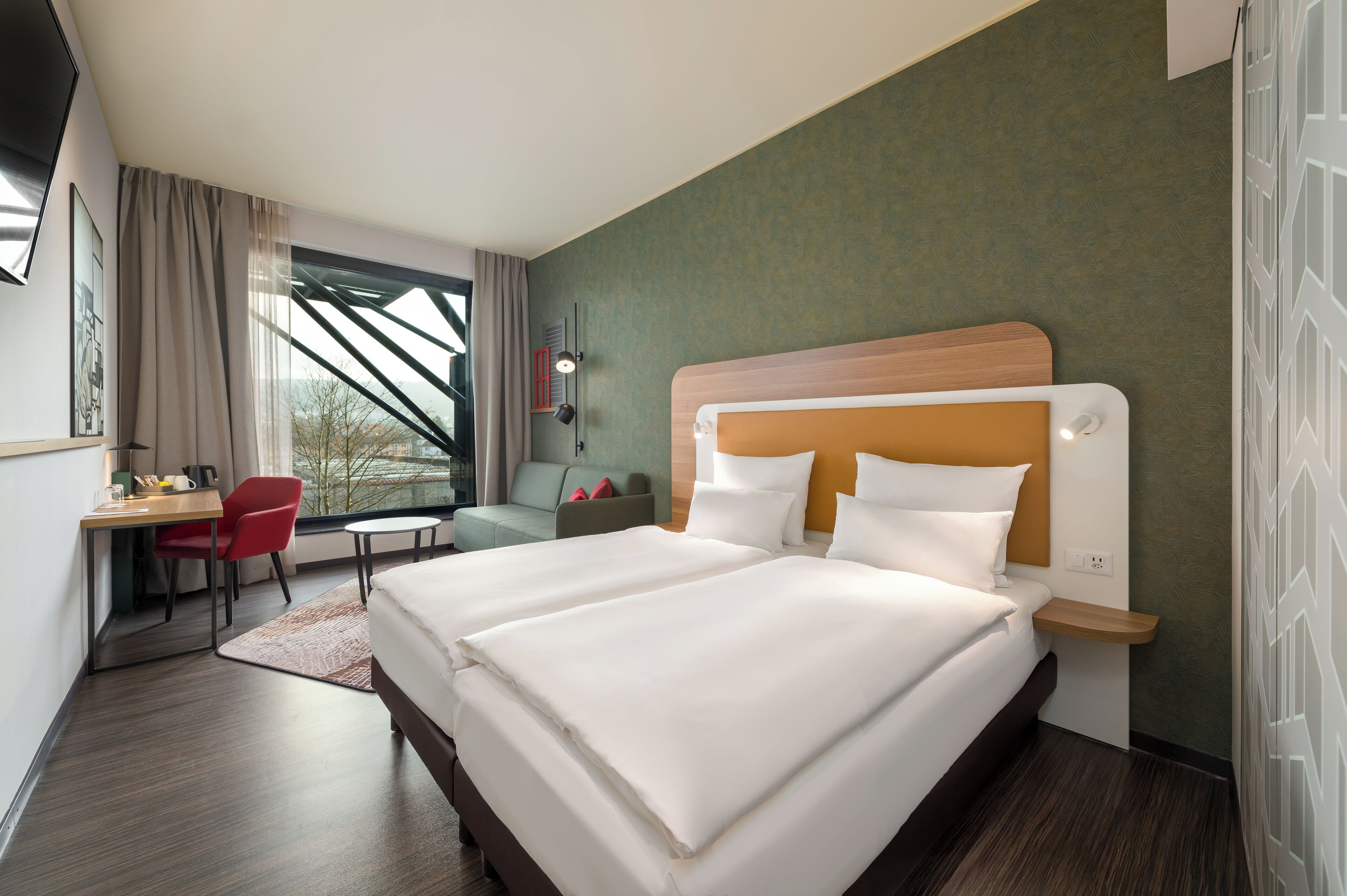 A hotel room with a large bed, a desk, a chair, and a view of the outdoors.