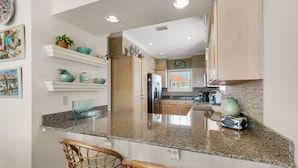A kitchen with granite countertops, wooden cabinets, and a central island with two wicker chairs.