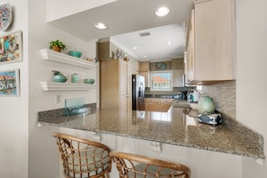A kitchen with granite countertops, wooden cabinets, and a central island with two wicker chairs. - Jen's Creole 4 Bedroom Townhouse by RedAwning (Navarre)