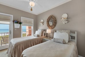 A bedroom with two beds, a ceiling fan, a wall-mounted mirror, and a view of the ocean through a sliding door. - Jen's Creole 4 Bedroom Townhouse by RedAwning (Navarre)