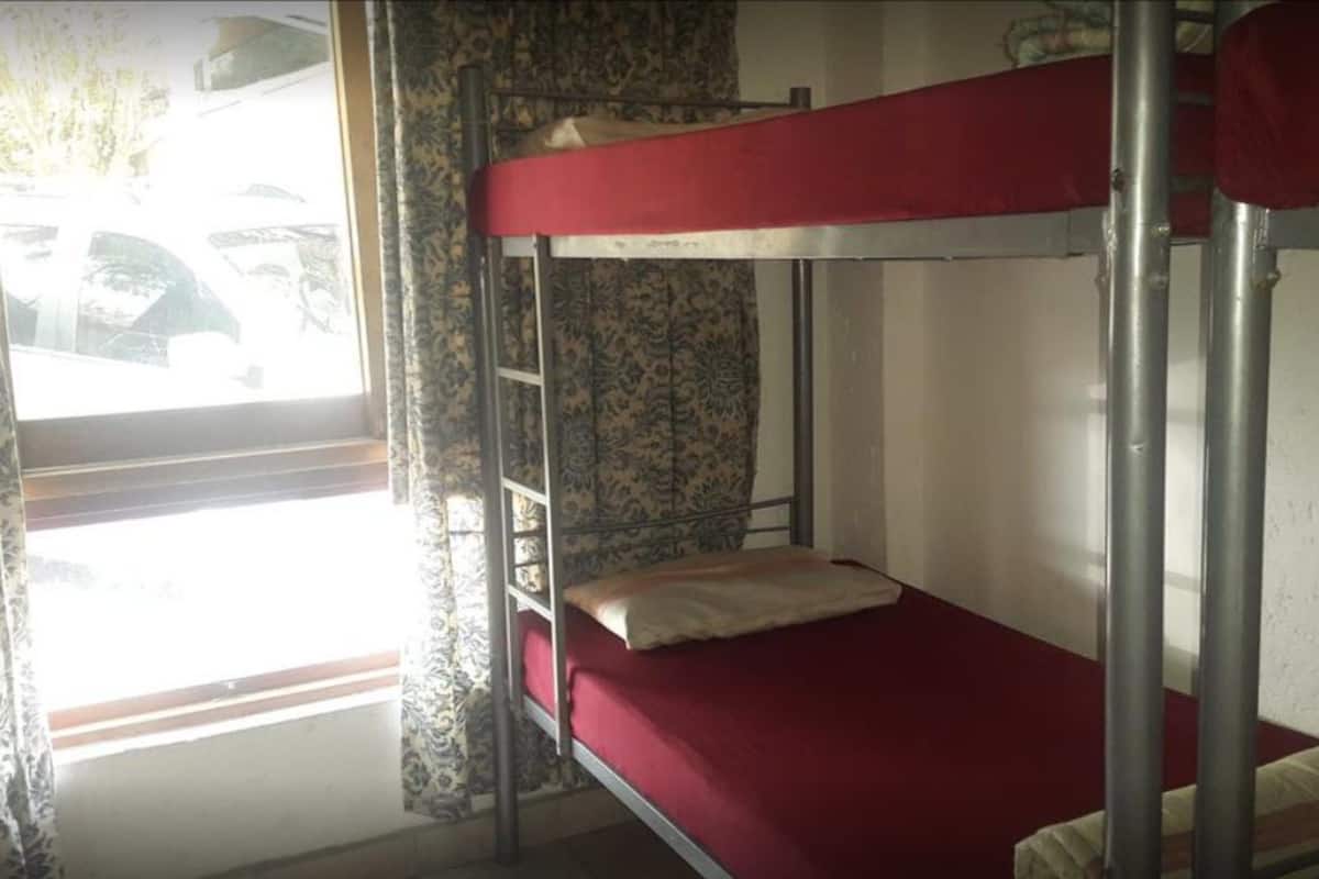 Une chambre avec un lit superposé, une fenêtre, des rideaux et un mur décoré de motifs.