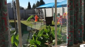 A room with a large window, a bed with a patterned blanket, and a view of an outdoor area with a blue tarp and some outdoor furniture. - Johannesburg Youth Hostel (Randburg)