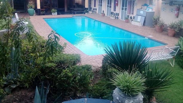 A swimming pool surrounded by potted plants and a covered seating area. - Johannesburg Youth Hostel (Randburg)
