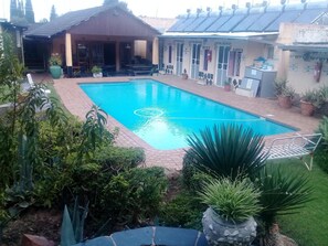 A swimming pool surrounded by potted plants and a covered seating area. - Johannesburg Youth Hostel (Randburg)