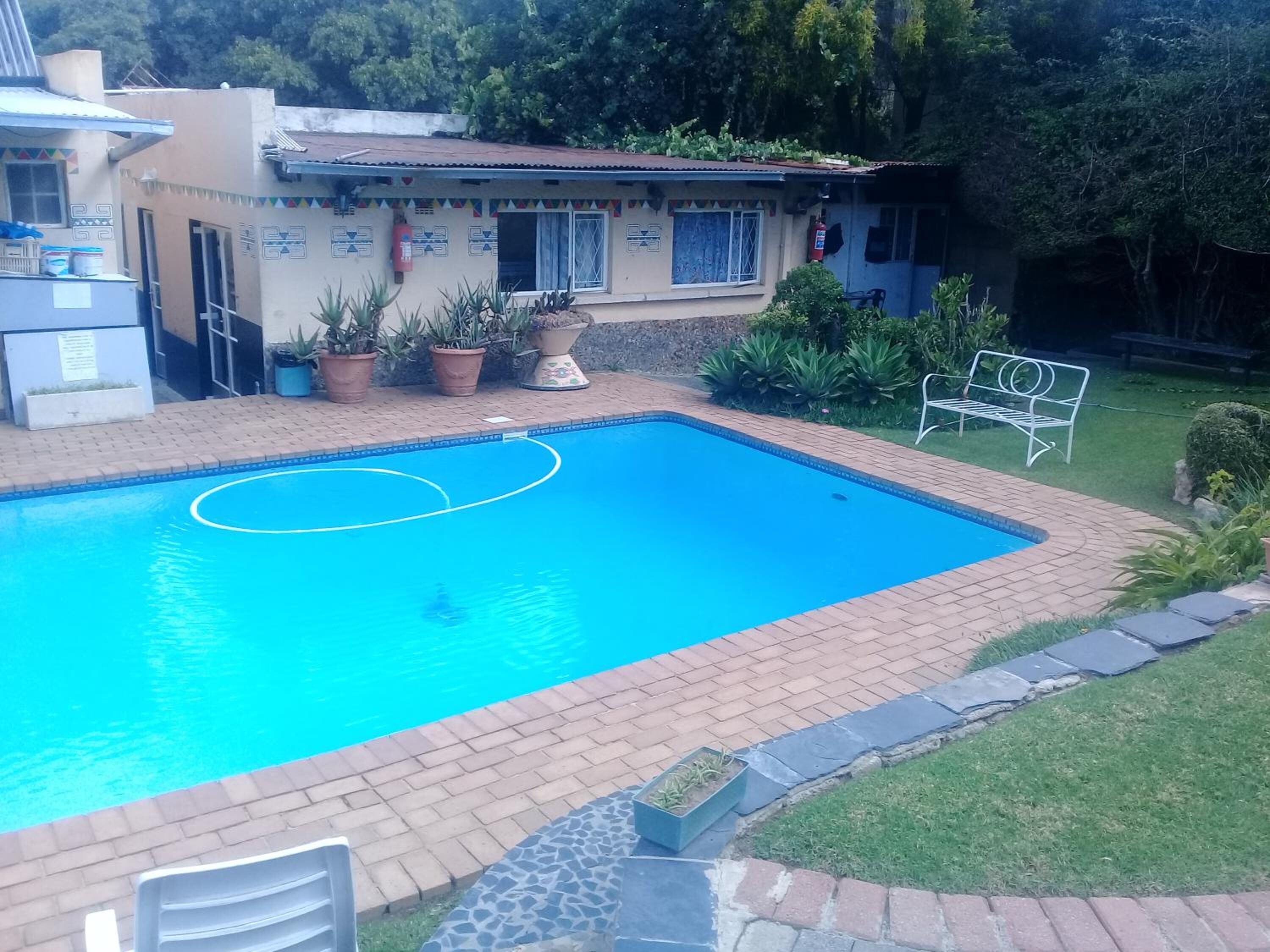 A rectangular swimming pool with a tiled border, surrounded by a brick patio. There are potted plants and a metal bench near the pool.