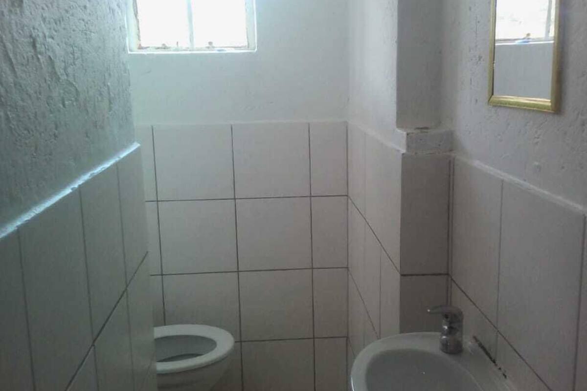 Een kleine, eenvoudige badkamer met toilet en wastafel, betegelde wanden en een raam voor natuurlijk licht.