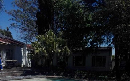 A clear blue swimming pool with a brick edge, surrounded by trees and a building in the background.