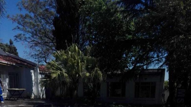 A clear blue swimming pool with a brick edge, surrounded by trees and a building in the background. - Fourways Youth Hostel (Sandton)