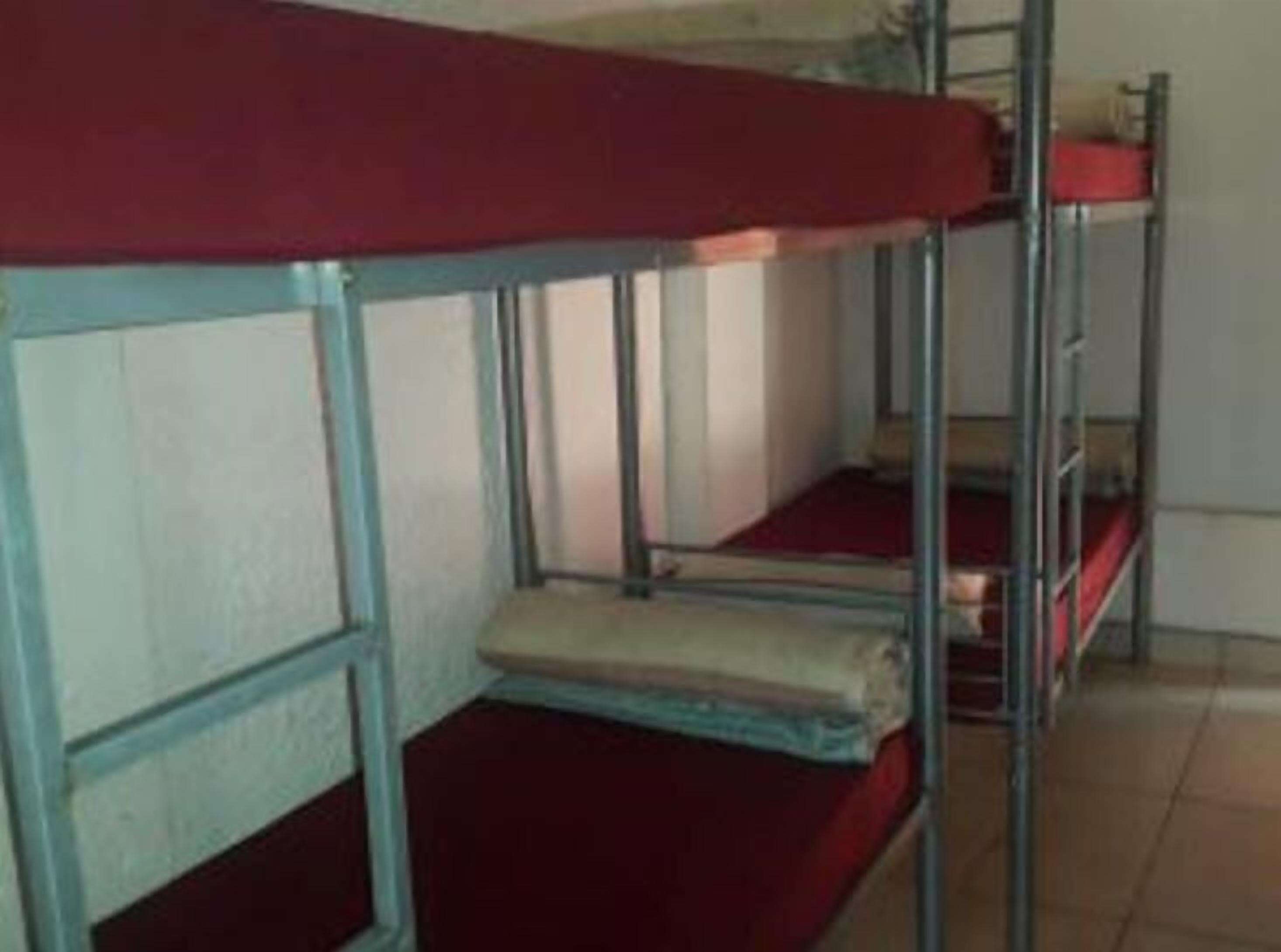 Dormitorio con literas, barandillas de metal y ropa de cama roja.