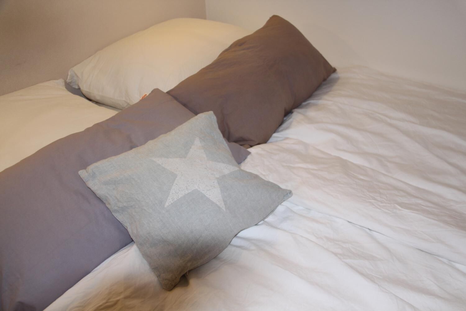 A bed with white bedding and three pillows in different shades.