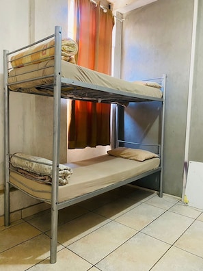 Una cama litera de dos plazas, una ventana con cortinas y suelo de baldosas.