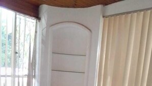 Un dormitorio con cama, mesita de noche, ventana con cortinas y estante en la pared.