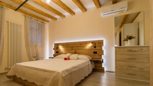 A bedroom with a wooden headboard, a bed with a white bedspread, a bedside table with a vase of flowers, and a wooden dresser. - Bragora 3524 Between S. Marco & Biennale (Venice)