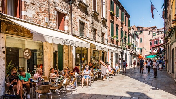 A street with outdoor seating at cafes, a brick building, and a clear sky. - Bragora 3524 Between S. Marco & Biennale (Venice)