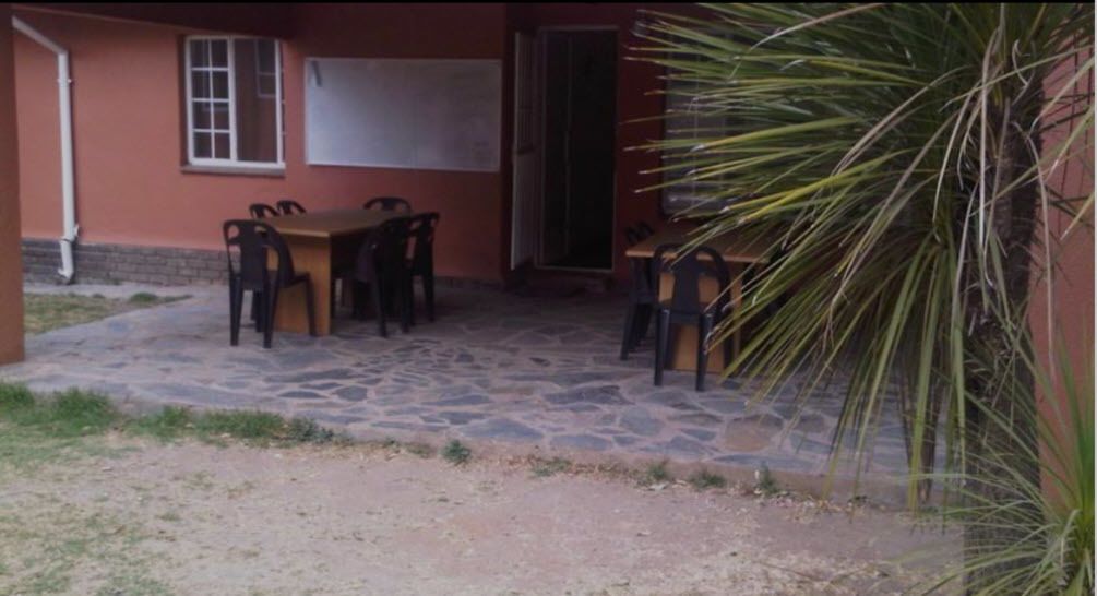 Een terras met een stenen vloer, een houten tafel en stoelen.