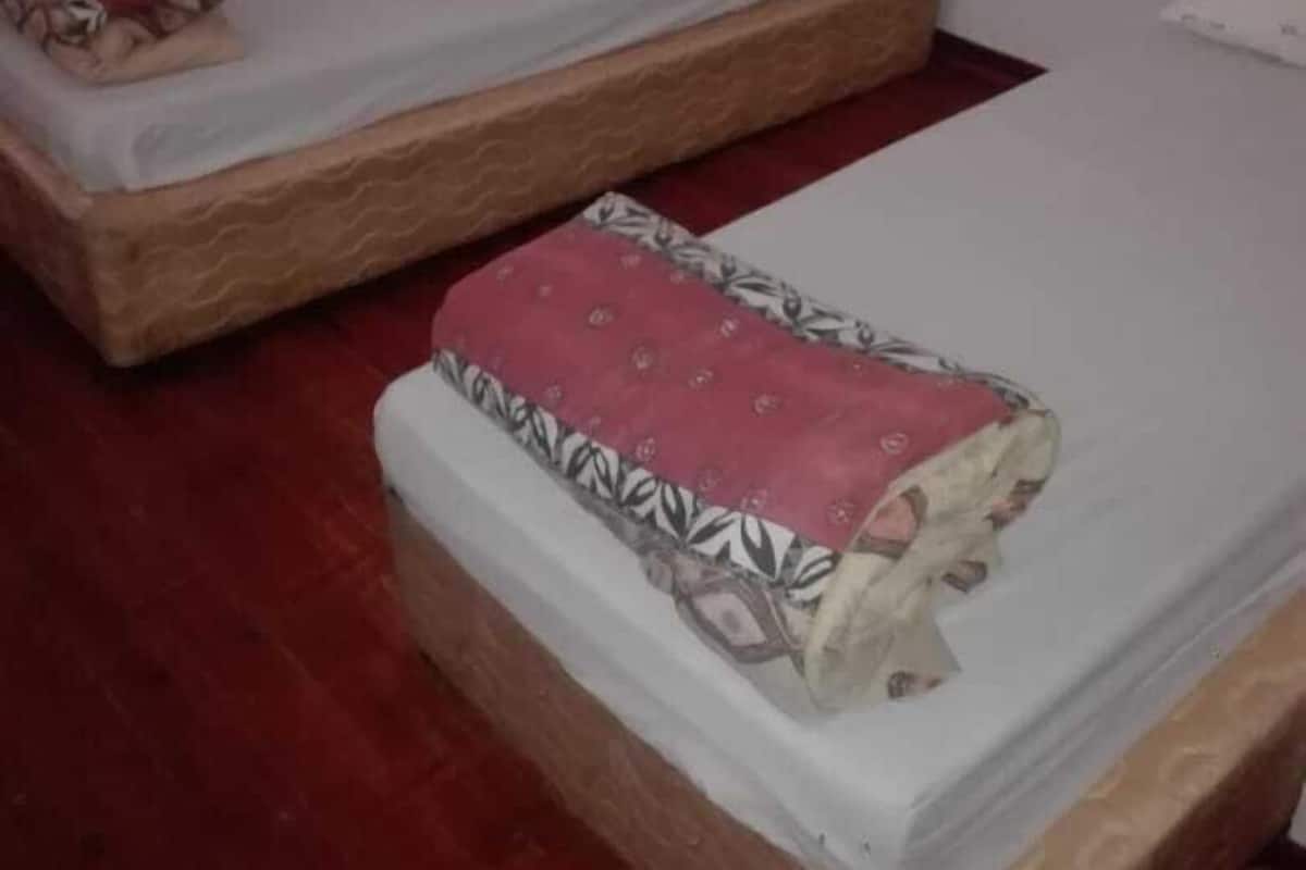 Two single beds with wooden frames and white mattresses, one with a red blanket and the other with a patterned blanket.