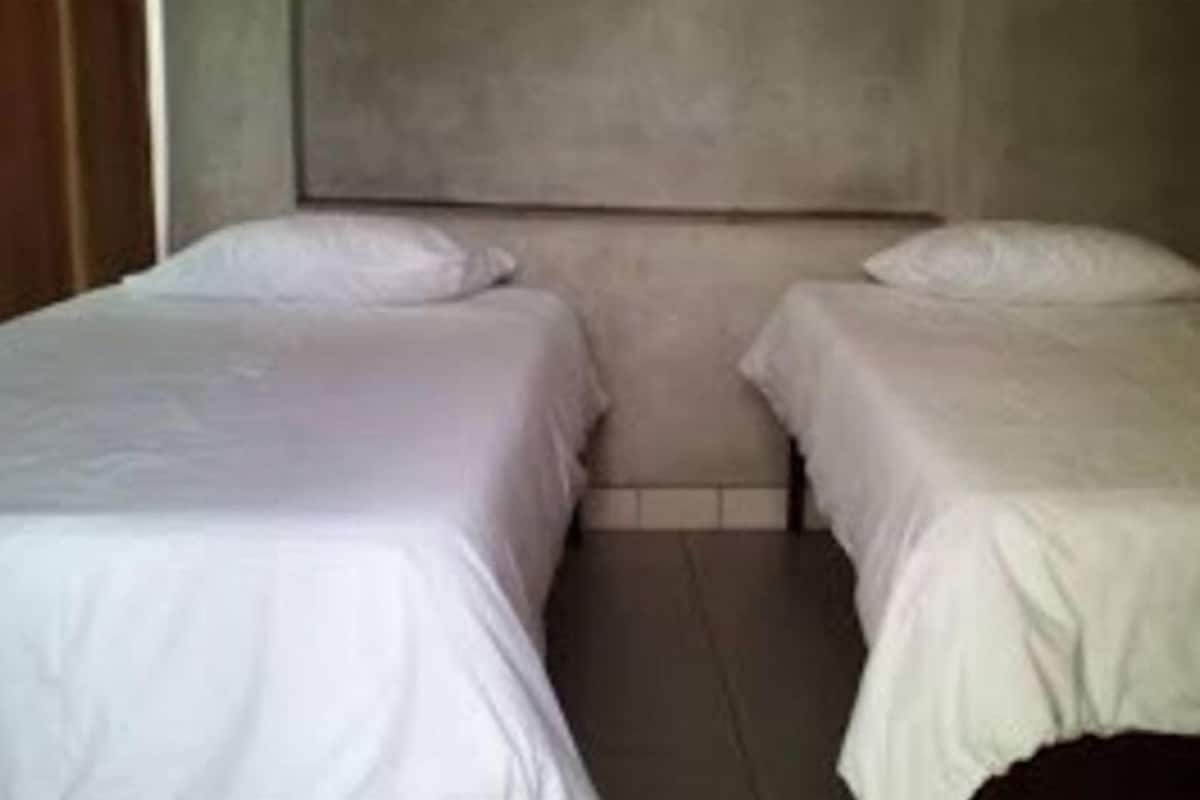 A room with two single beds, a plain wall, and a tiled floor.