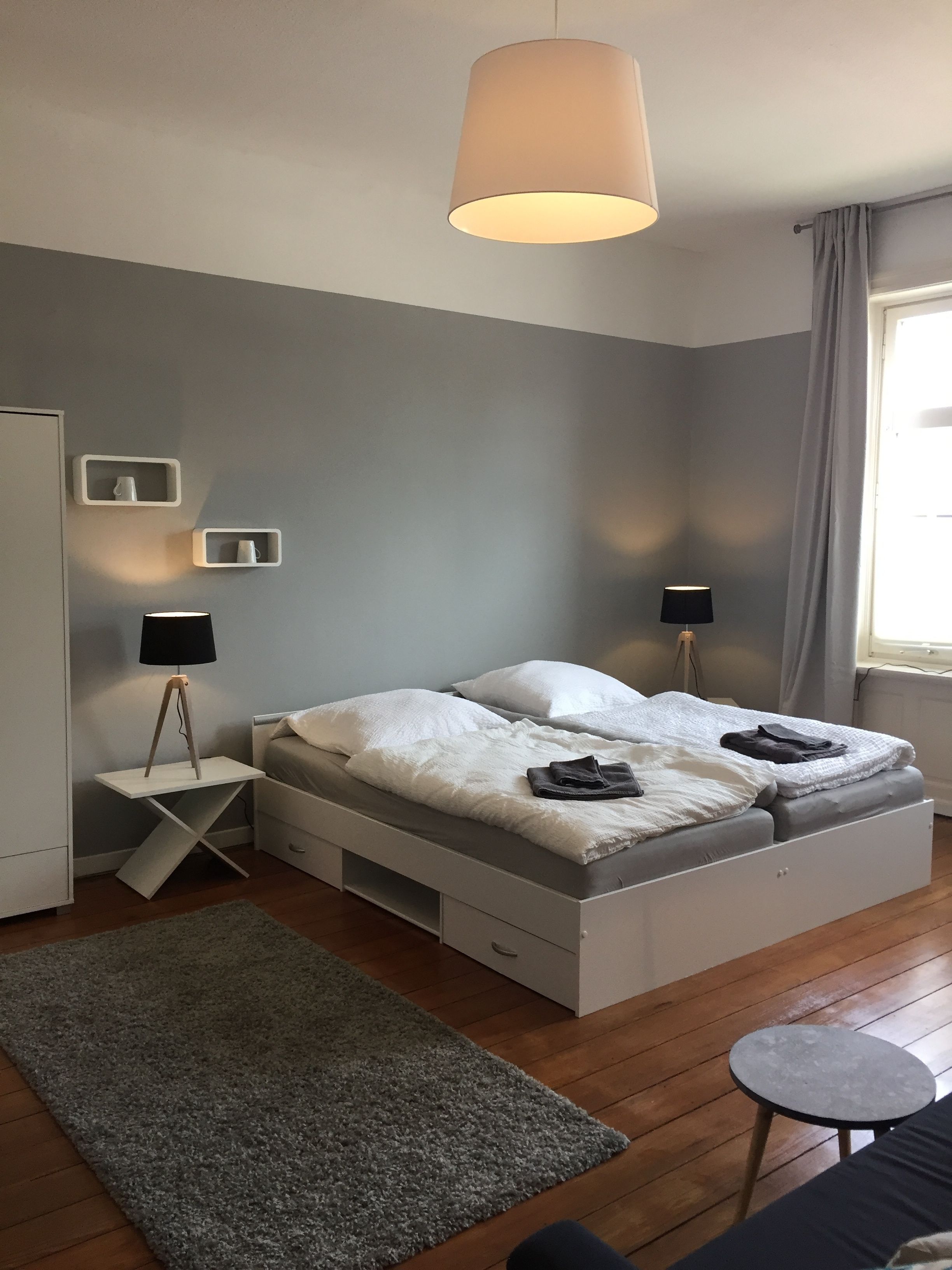 A modern bedroom with a bed, bedside tables, a desk, a small round table, and a grey carpet.