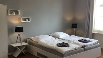 A modern bedroom with a bed, bedside tables, a desk, a small round table, and a grey carpet.