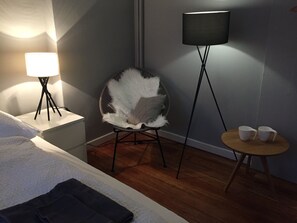A hotel room with a bed, a chair with a fluffy cushion, a standing lamp, and a small table with two cups. - Nice n Nordic 2 (Hamburg)