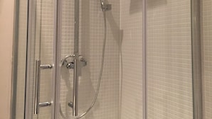 Et brusebad med glasvægge, en håndbruser og en fastmonteret brusearmatur.