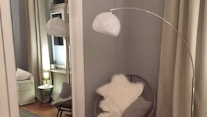 Et hjørneværelse med en rund stol, gulvlampe, spejl og en grå måtte.