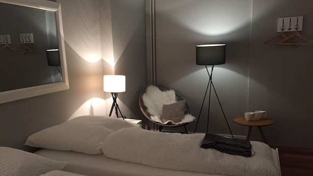 Et hotelværelse med en seng, en stol, et lille bord og to gulvlamper.