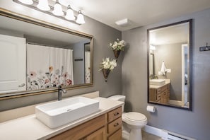 Une salle de bain avec un lavabo blanc, un meuble-lavabo en bois, deux miroirs fixés au mur et des toilettes.