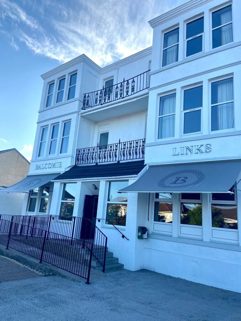 Un edificio blanco de varios pisos, con balcones y toldos con señalización.