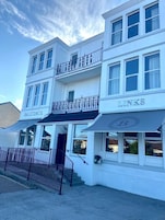 A white building with multiple stories, featuring balconies and awnings with signage.