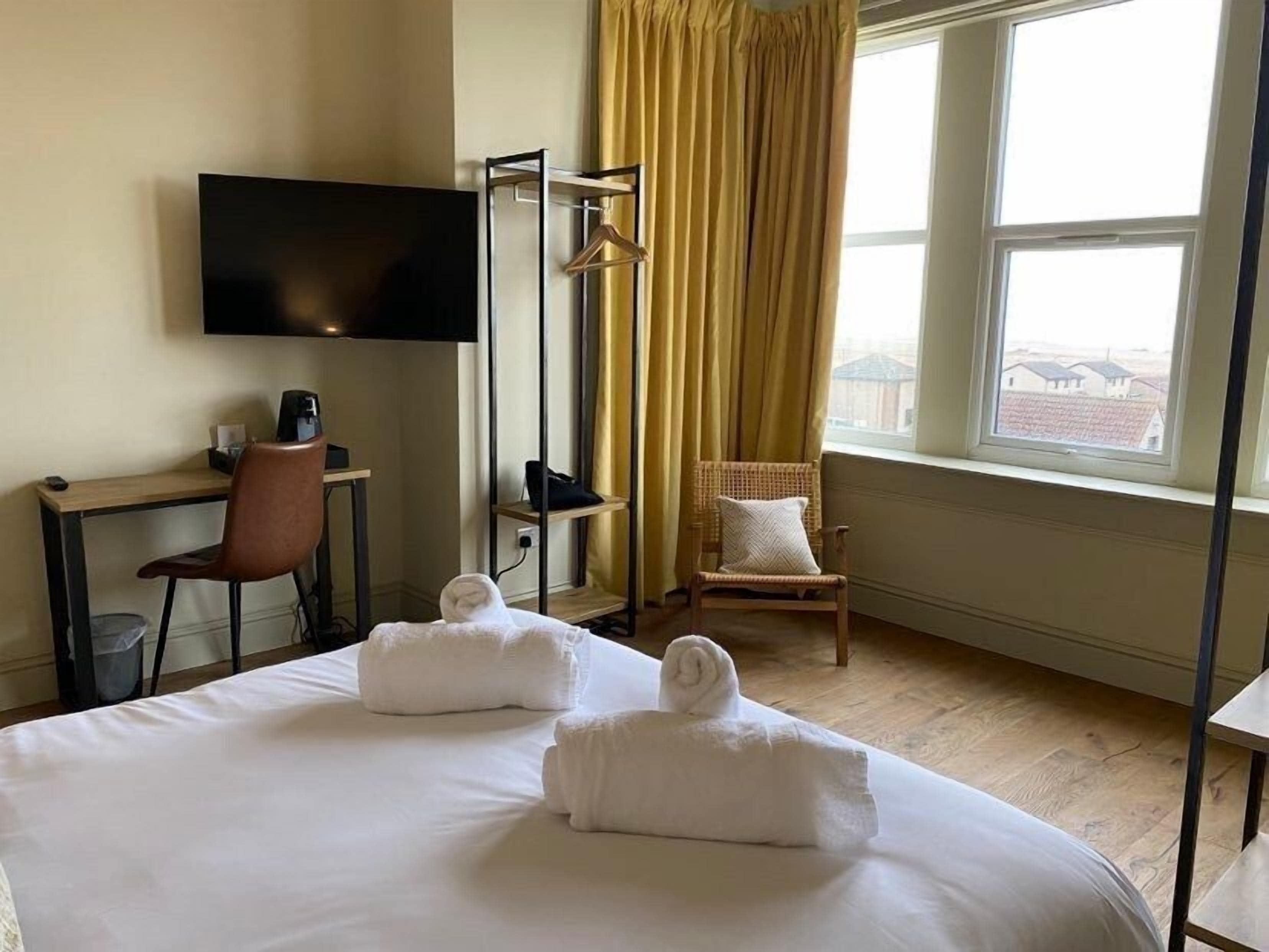 Ein Hotelzimmer mit Bett, Schreibtisch, Stuhl, Fernseher und einem Fenster mit Vorhängen.