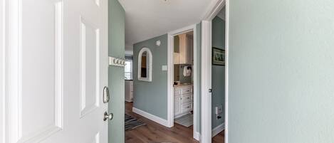 Un pasillo con una puerta blanca, una lámpara y un rug con rayas que conduce a un baño con un tocador blanco y un perchero.