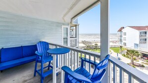 A balcony with blue furniture, a view of the ocean, and a building in the background. - Seascape 2309 2 Bedroom Condo by RedAwning (Galveston)