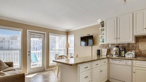 A kitchen with white cabinets, a built-in dishwasher, and a flat-screen TV mounted above the counter.