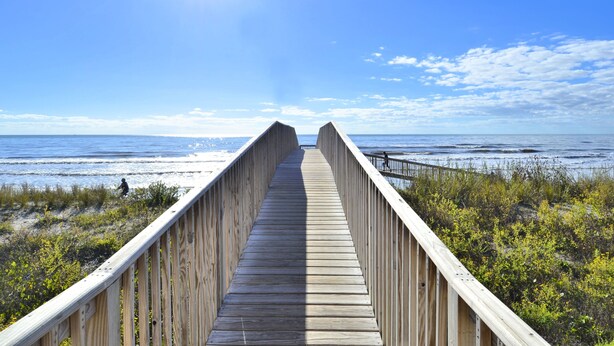 A wooden boardwalk leading to the beach with a clear view of the ocean and sky.