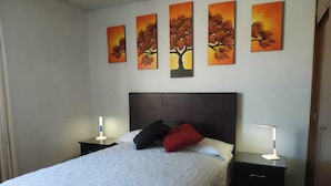A bedroom with a bed, two bedside tables, and four wall-mounted paintings. - DEPARTAMENTO PISO 20a, CENTRICO, CERCA EMBAJADA AMERICANA, TELEFERICO, MALLS, VISTAS PANORAMICAS y SEGURO (La Paz)