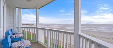 A covered porch with blue chairs and a view of the beach.