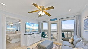 Un vaste espace de vie doté d’un ventilateur de plafond, d’un grand téléviseur à écran plat, d’un canapé et d’un balcon offrant une vue sur la plage.
