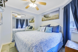 A bedroom with two beds, a ceiling fan, a large mirror, and artwork on the wall.