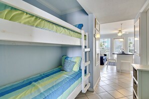 A bunk bed room with a kitchen area in the background. - Seascape 1120 Studio Bedroom Condo by RedAwning (Galveston)