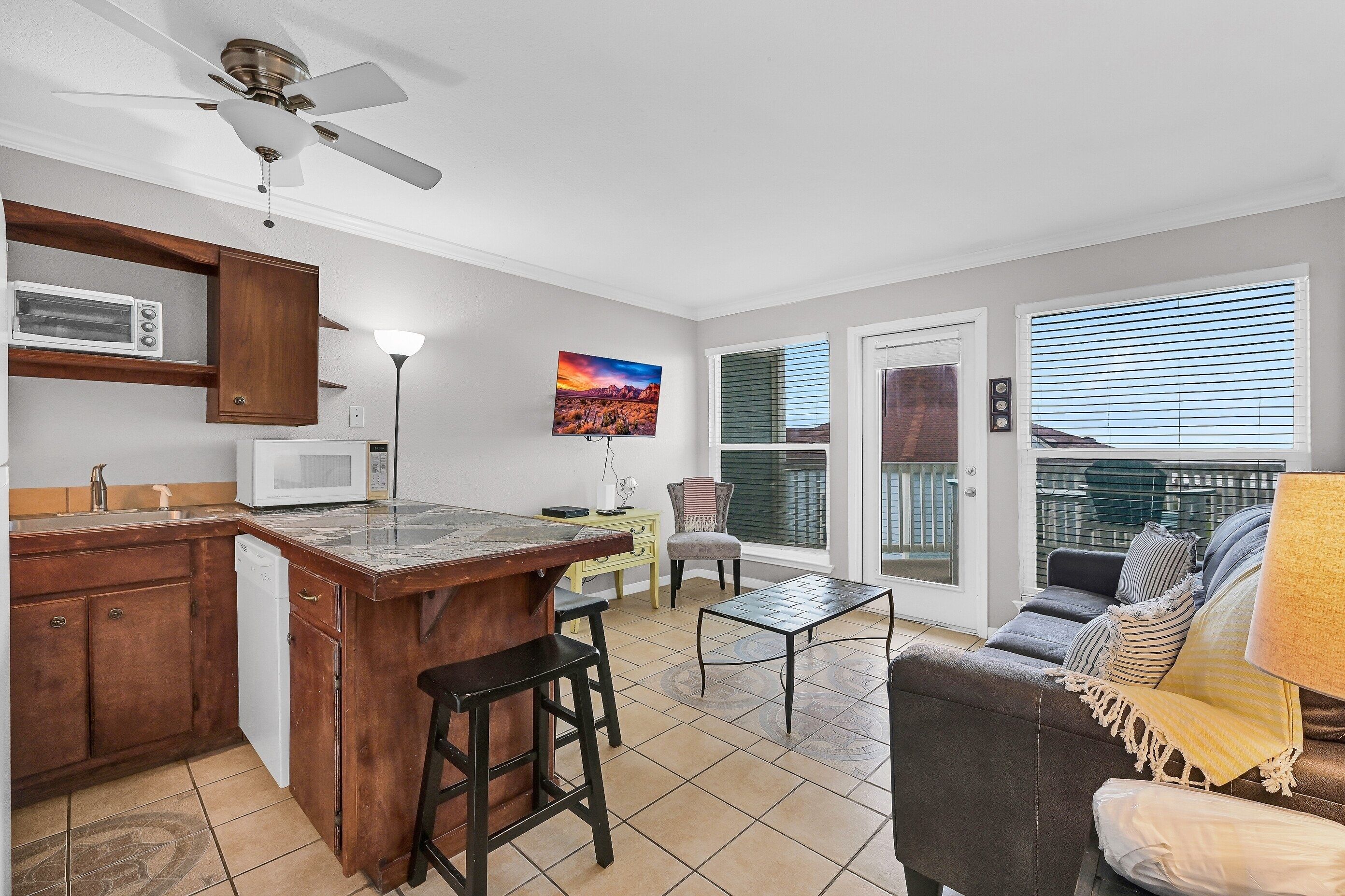 A kitchen with a microwave, wooden cabinets, a bar stool, a dining table, and a TV.