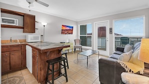 Una cocina con microondas, armarios de madera, un taburete de bar, una mesa de comedor y un televisor.