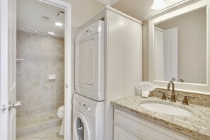 A bathroom with a washing machine, a sink, and a shower.