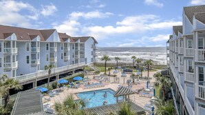 A hotel with a pool area, including lounge chairs and umbrellas, overlooking the ocean.