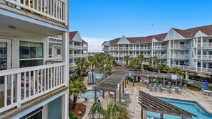A hotel with multiple balconies, a pool area with lounge chairs, and a small hot tub. - Seascape 1214 Studio Bedroom Condo by RedAwning (Galveston)
