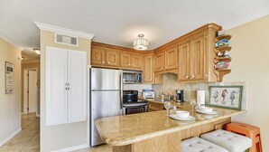 A kitchen with wooden cabinets, a stainless steel refrigerator, a built-in oven, and a granite countertop. - Seascape 1214 Studio Bedroom Condo by RedAwning (Galveston)