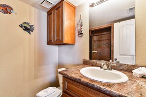 A bathroom with a granite countertop sink, wooden cabinets, and decorative fish wall art.