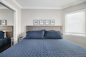 A bedroom with a large bed, a wooden headboard, a nightstand, a mirror, and a window with blinds.