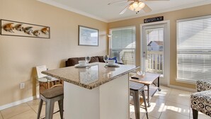 A kitchen with a central island, bar stools, a ceiling fan, and a dining area with a sofa and chairs.